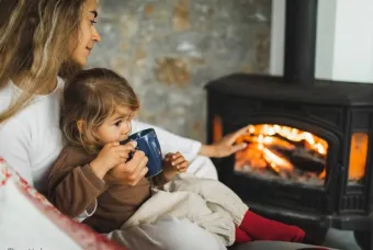 Vrouw met kind op schoot voor de kachel